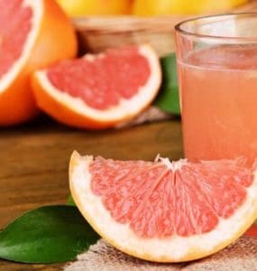 Eine Scheibe Grapefruit neben einem Glas frisch gepresstem Grapefruitsaft