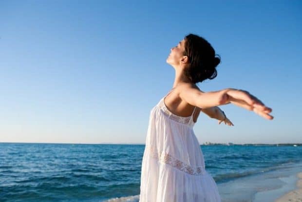 Frau mit geweiteten Armen steht am Strand