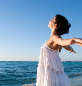 Frau mit geweiteten Armen steht am Strand