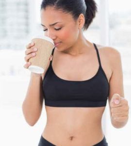 Dunkelhaarige Frau im Sportdress mit Kaffeebecher in der rechten Hand