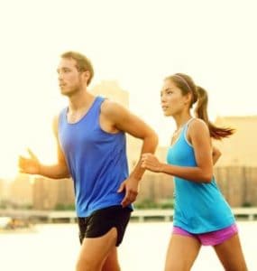 Junger Mann und junge Frau mit blauen T-Shirts joggen nebeneinander mit optimalem Trainingspuls