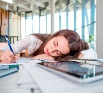 NAchmittagstief: Junge Frau im Büro liegt mit dem Kopf auf dem Schreibtisch und schläft