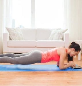 Frau macht eine Plank im Wohnzimmer auf einer Yogamatte vor einer Couch