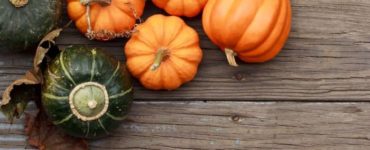 Vier orange und ein grüner Kürbis auf einem Holztisch