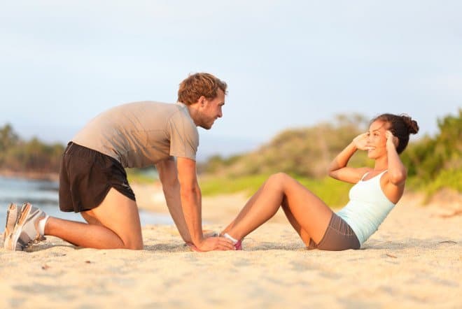 Mann und frau am Sandstrand machen Sit Ups