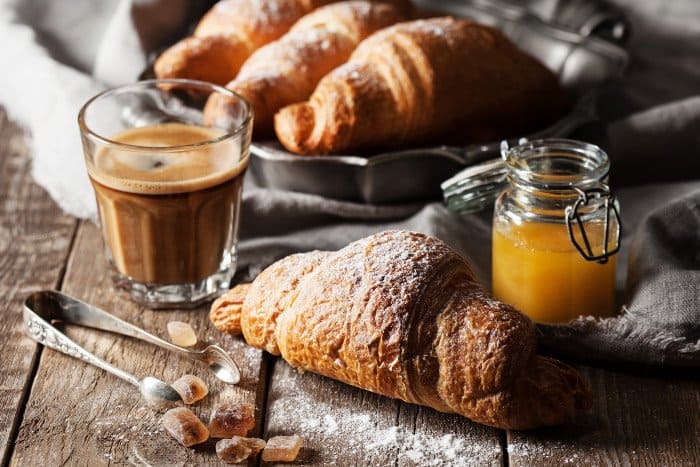 Croissant in Mehl auf Holztisch mit Glas Kaffee.