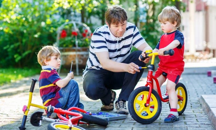 Vater repariert mit seinen beiden Kindern ein Kinderrad.