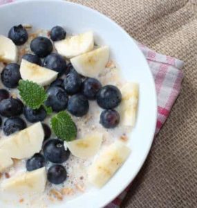 Keramikschüssel gefüllt mit Bananenstückchen, Blaubeeren und Molke, dazu etwas Minze