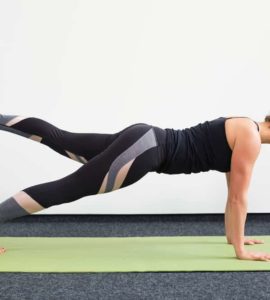 Junge Frau in Liegestützposition auf einer hellgrünen Trainingsmatte macht Pilates Leg Pull Front