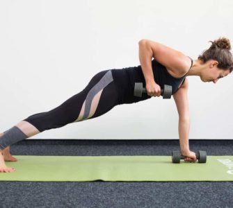 Junge Frau in Liegestützposition auf einer hellgrünen Trainingsmatte zieht mit Kurzhanteln einen Arm hoch