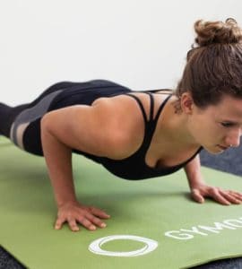 Junge Frau in Liegestützposition auf einer hellgrünen Trainingsmatte macht Push Ups