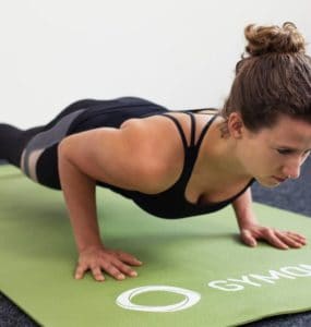 Junge Frau in Liegestützposition auf einer hellgrünen Trainingsmatte macht Push Ups