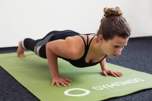 Junge Frau in Liegestützposition auf einer hellgrünen Trainingsmatte macht Push Ups