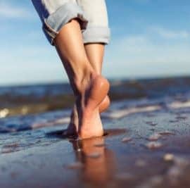 Frau läuft am Strand barfuß durch den Sand, denn barfußlaufen ist gesund