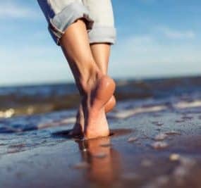 Frau läuft am Strand barfuß durch den Sand, denn barfußlaufen ist gesund