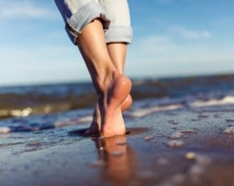 Frau läuft am Strand barfuß durch den Sand, denn barfußlaufen ist gesund