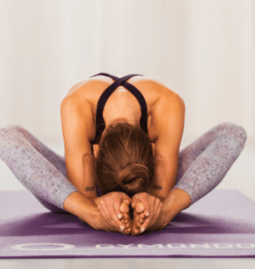 Valerie Junger sitzt im Schneidersitz auf einer lila Trainingsmatte von Gymondo und macht Yin Yoga