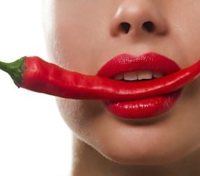 Frau mit Chilischote im Mund mit Lippenstift