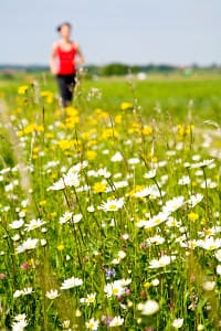 Eine Frau joggt über einen Feldweg mit Gräsern, die Heuschnupfen auslösen können.