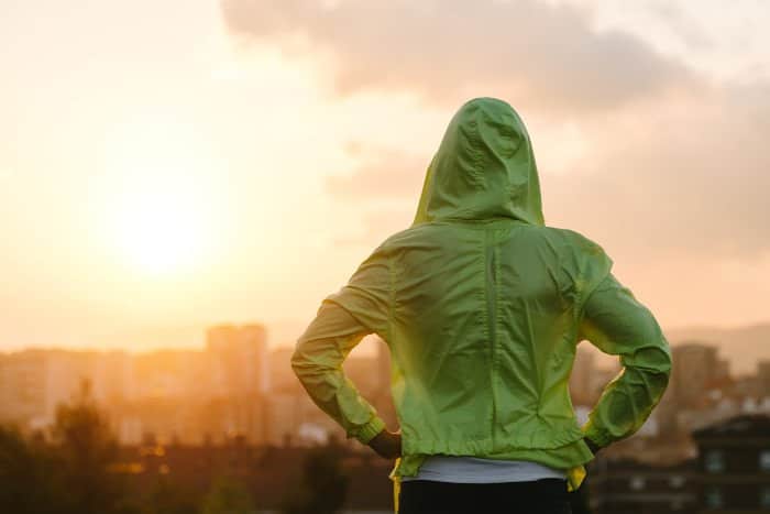 Frau mit grünem Kapuzenpulli schaut in den Sonnenuntergang.