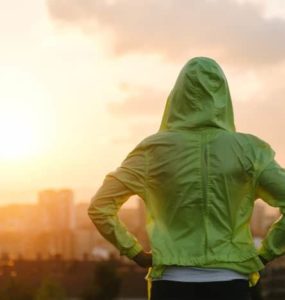 Frau mit grünem Kapuzenpulli schaut in den Sonnenuntergang.