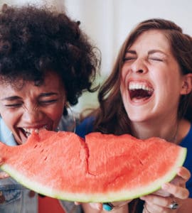 Zwei junge Frauen lachen und essen zusammen ein großes Stück Wassermelone