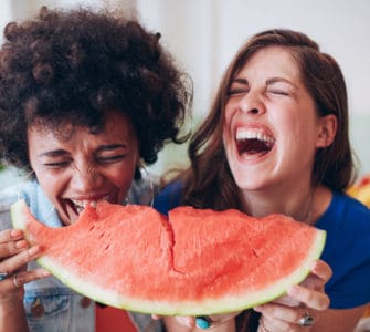 Zwei junge Frauen lachen und essen zusammen ein großes Stück Wassermelone