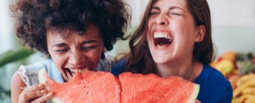 Zwei junge Frauen lachen und essen zusammen ein großes Stück Wassermelone