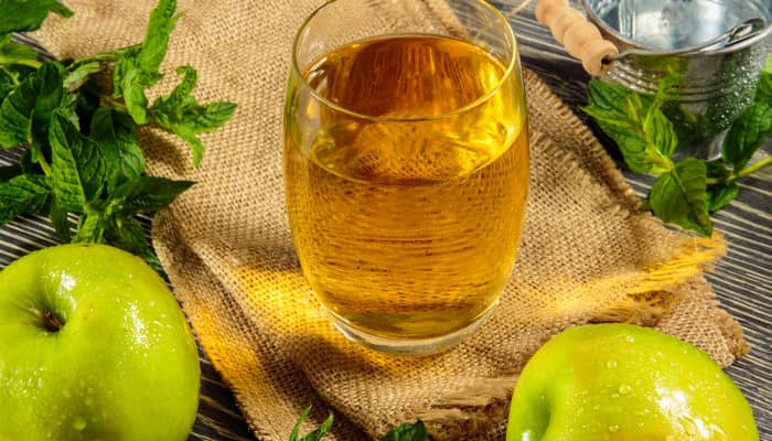 Glas Apfelsaft neben zwei grünen Äpfeln