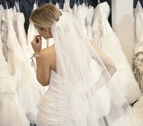 Frau in Brautkleid vor einer Kleiderstange mit vielen weiteren Brautkleidern