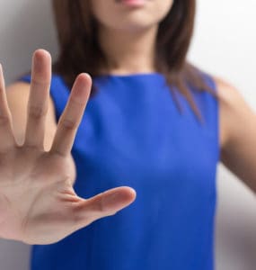 Frau in blauem Kleid streckt die Hand nach vorne und sagt Nein