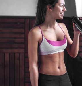 Frau in Sportkleidung trinkt aus einer Flasche nach dem Fitnesstraining