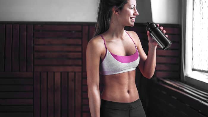 Frau in Sportkleidung trinkt aus einer Flasche nach dem Fitnesstraining