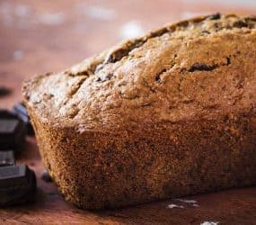 Ein Schokoladen-Zucchini-Kuchen mit danebenliegender Zucchini sowie Stücken dunkler Schokolade