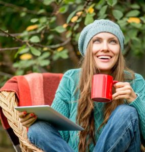 Junge Frau mit Mütze sitzt draußen in der Natur mit einer Tasse Mate Tee