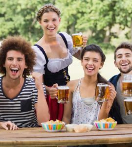 Gruppe junger Menschen sitzen an einem Holztisch und trinken Bier auf dem Oktoberfest