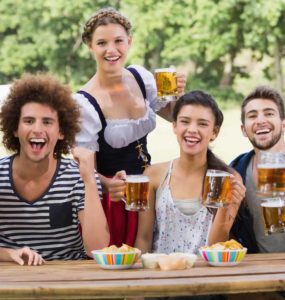 Gruppe junger Menschen sitzen an einem Holztisch und trinken Bier auf dem Oktoberfest