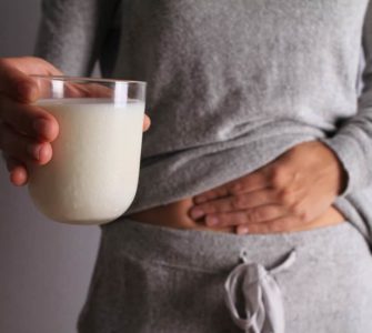 Frau mit Milchglas in der Hand fasst sich an den Bauch, hat Blähungen durch Laktoseintoleranz