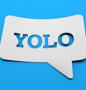 weißes schild mit YOLO in sprechblasenform vor blauem Hintergrund