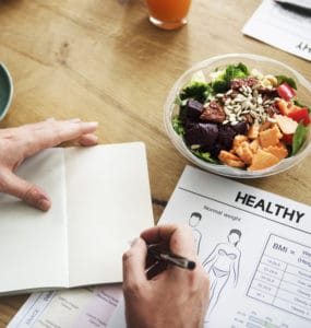 Ein Notizbuch mit Aufzeichnungen zu einer geusnden Ernährung auf einem Tisch mit gesundem Essen