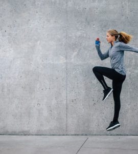 Junge Frau in sportlichem Outfit trainiert vor grauer Steinwand. Sie macht HIIT, den Fitness Trends 2018