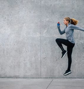 Junge Frau in sportlichem Outfit trainiert vor grauer Steinwand. Sie macht HIIT, den Fitness Trends 2018