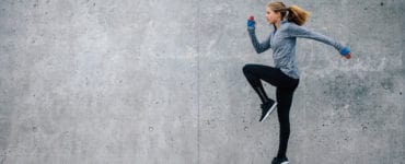 Junge Frau in sportlichem Outfit trainiert vor grauer Steinwand. Sie macht HIIT, den Fitness Trends 2018