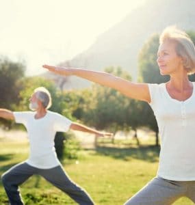 Eine Frau Mitte 50 und ihr Mann machen im Park Yogaübungen, denn Bewegung ist gesund