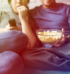 ein Paar sitzt auf dem Sofa und isst poppcorn und trinkt bier