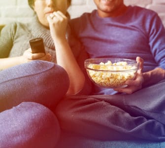 ein Paar sitzt auf dem Sofa und isst poppcorn und trinkt bier