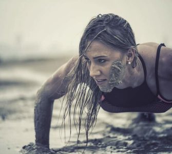 Trainierte Frau macht Crawling Fitness und krabbelt durch den Schlamm