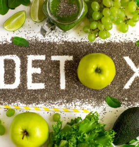 Tischplatte in der Mitte steht das Wort DETOX, darüber und darunter grünes Gemüse und Obst