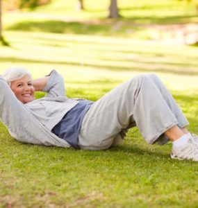 Ältere fitte Frau in Sportkleidung im Park liegt auf Wiese und macht Crunches