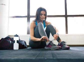 Übersäuerte Sportlerin mit Trinkflasche bindet sich die Schuhe